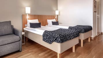 Ein Hotelzimmer mit einem Bett, zwei Nachttischen, einem grauen Sessel und Holzboden.