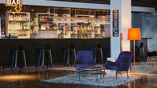 Zona de bar amb una varietat de garrafes de licors, gots i tamborets. Hi ha un mapa a la paret i una làmpada a la dreta.