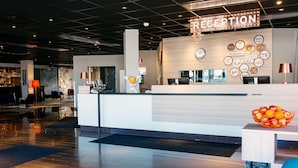 Zona d'entrada amb taulell de recepció, un rellotge i una paret amb diverses icones que indiquen serveis.