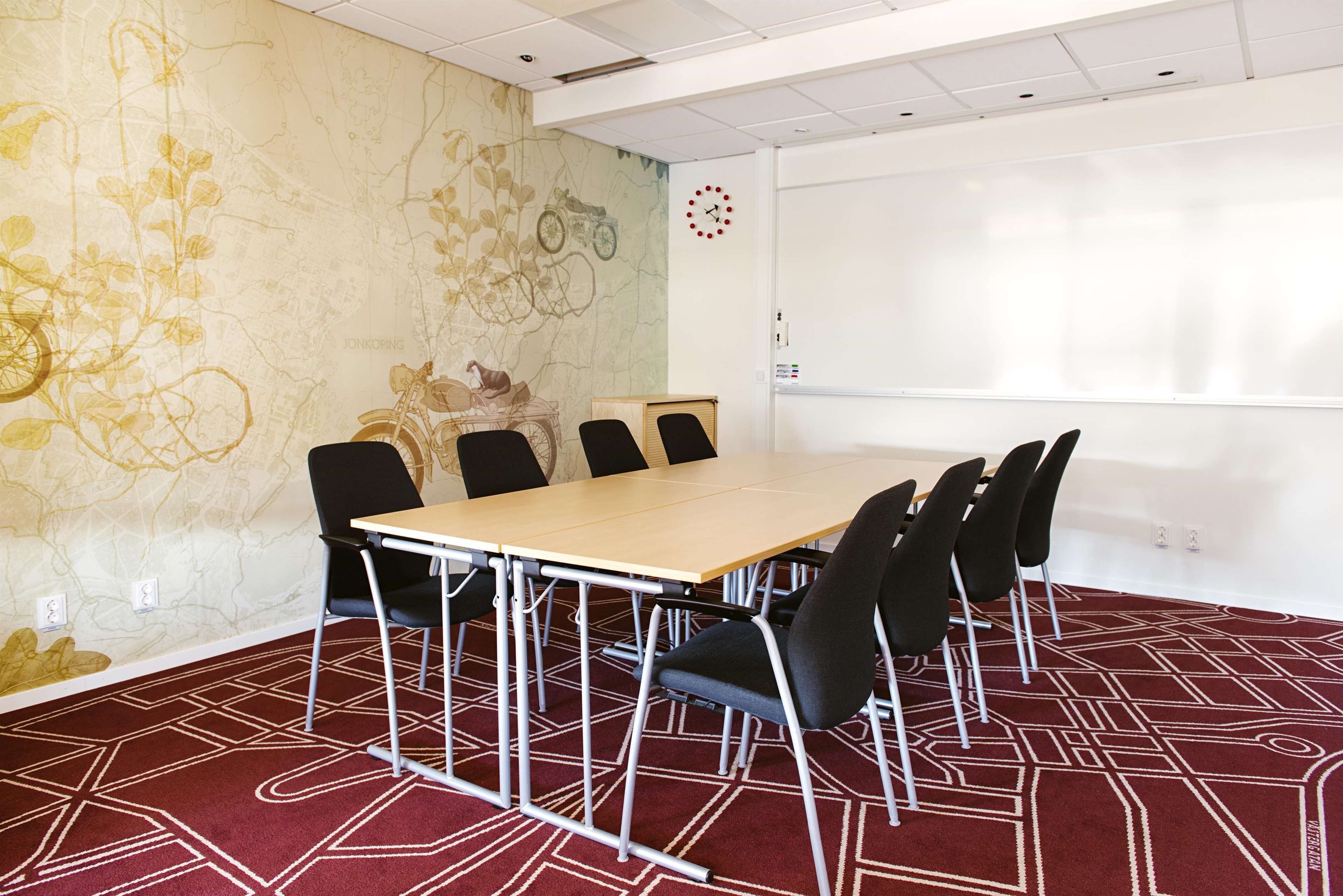 A conference room with a long table, black chairs, a whiteboard, and a clock on the wall.