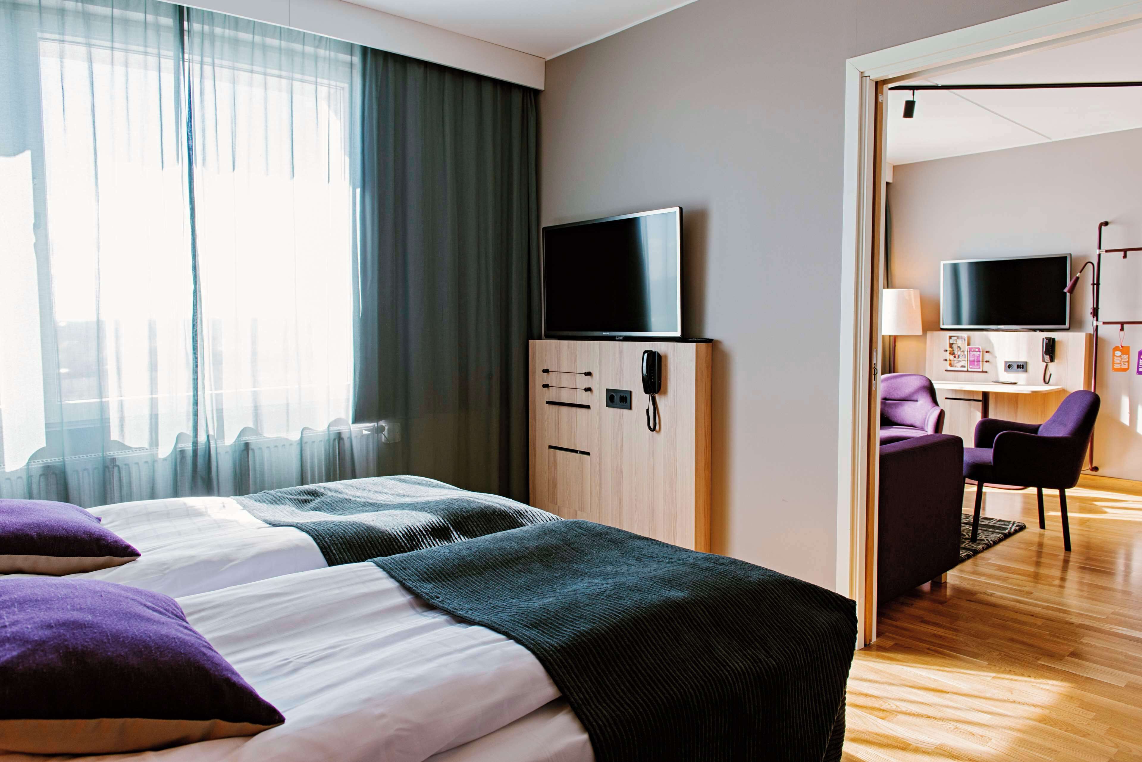 Habitación de hotel con dos camas, televisión, escritorio con silla y baño visible a través de una puerta abierta.