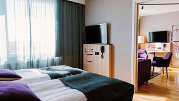 Habitación de hotel con dos camas, televisión, escritorio con silla y baño visible a través de una puerta abierta.
