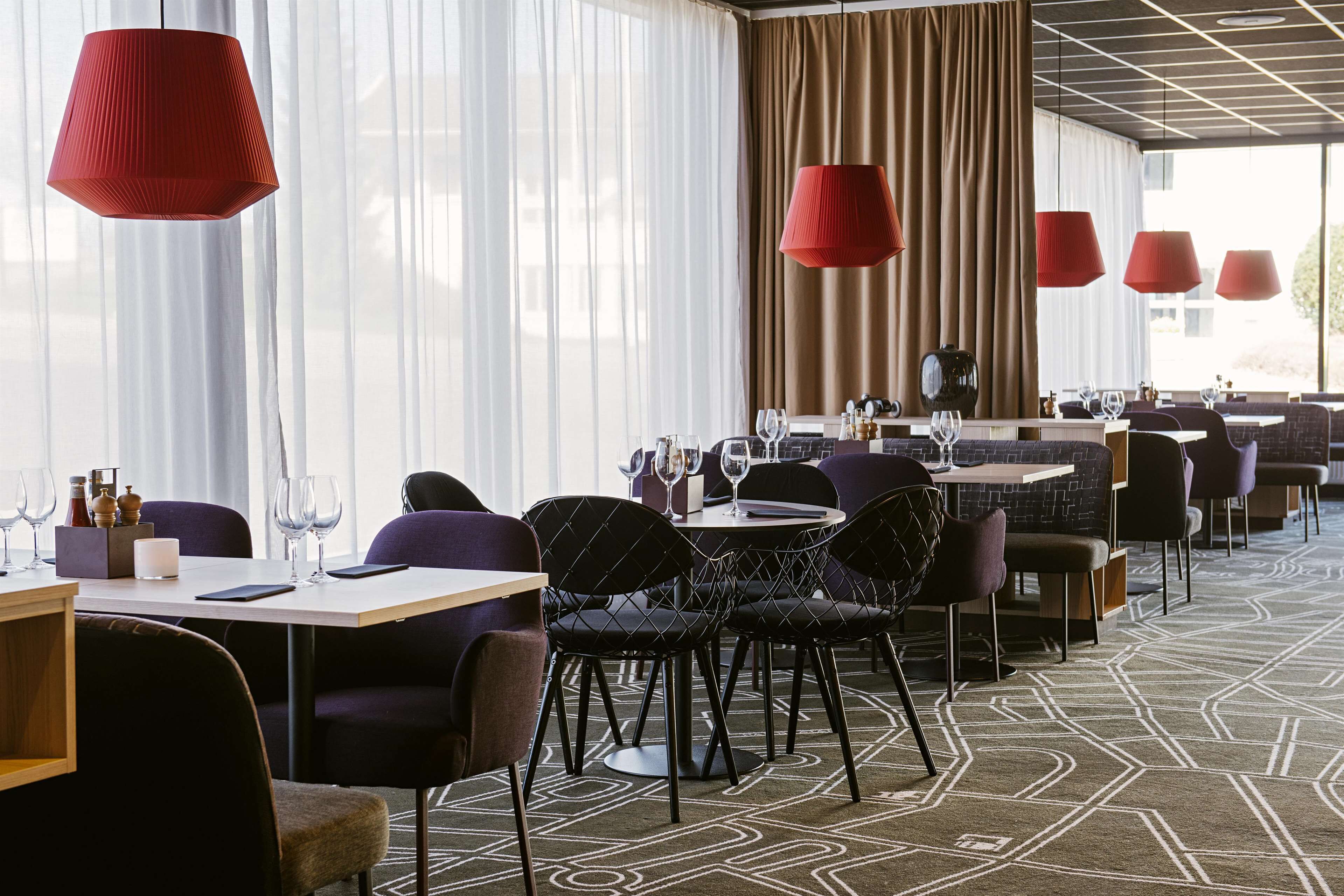 Un restaurante moderno con mesas redondas, sillas negras y lámparas colgantes rojas.
