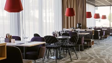 Un restaurante moderno con mesas redondas, sillas negras y lámparas colgantes rojas.