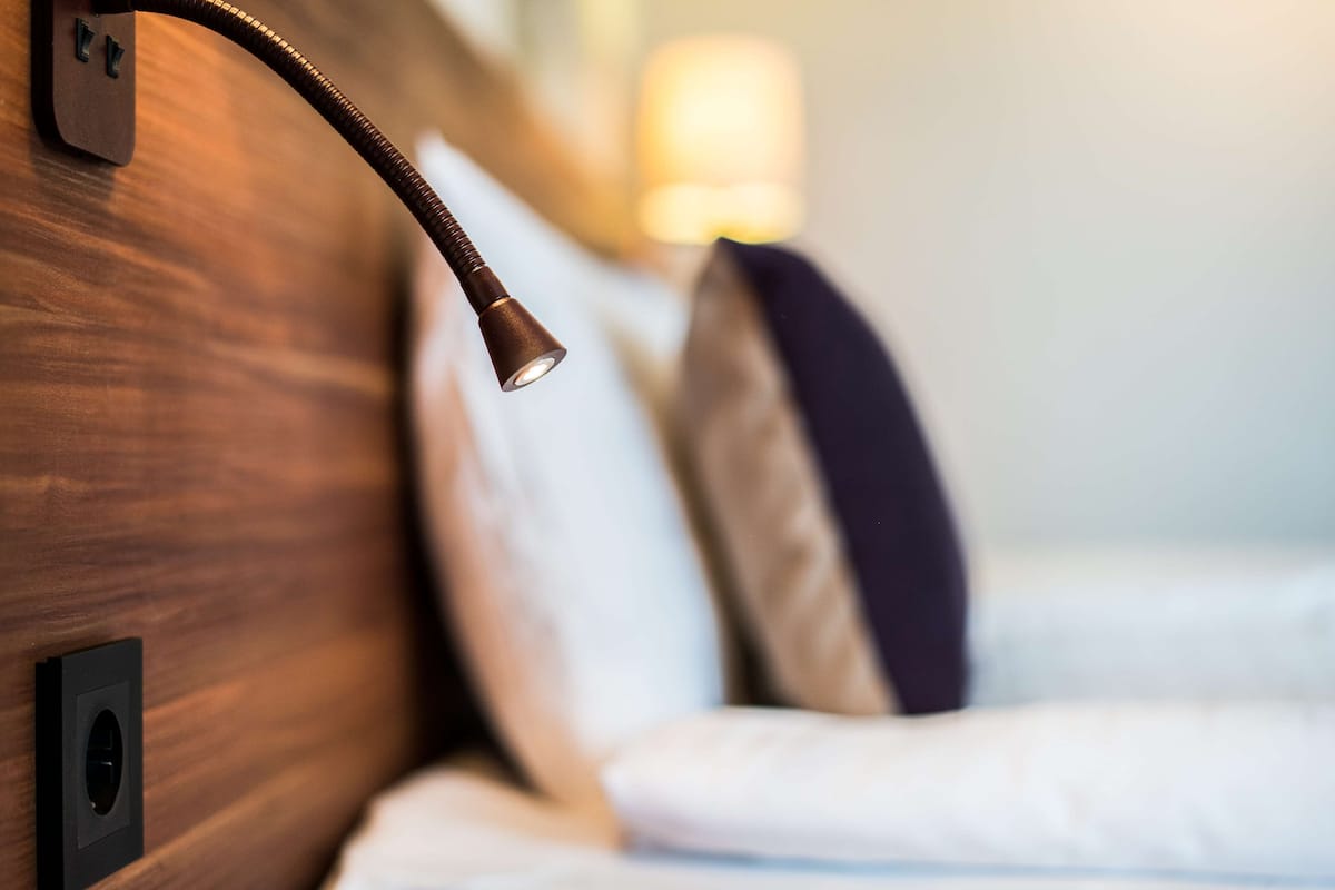 Een detail van een houten hoofdbord met een wandlamp en een stopcontact.