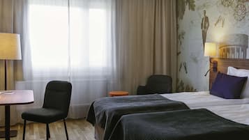 Habitación de hotel con cama, dos mesitas de noche, una silla, escritorio y ventana con cortinas traslúcidas.