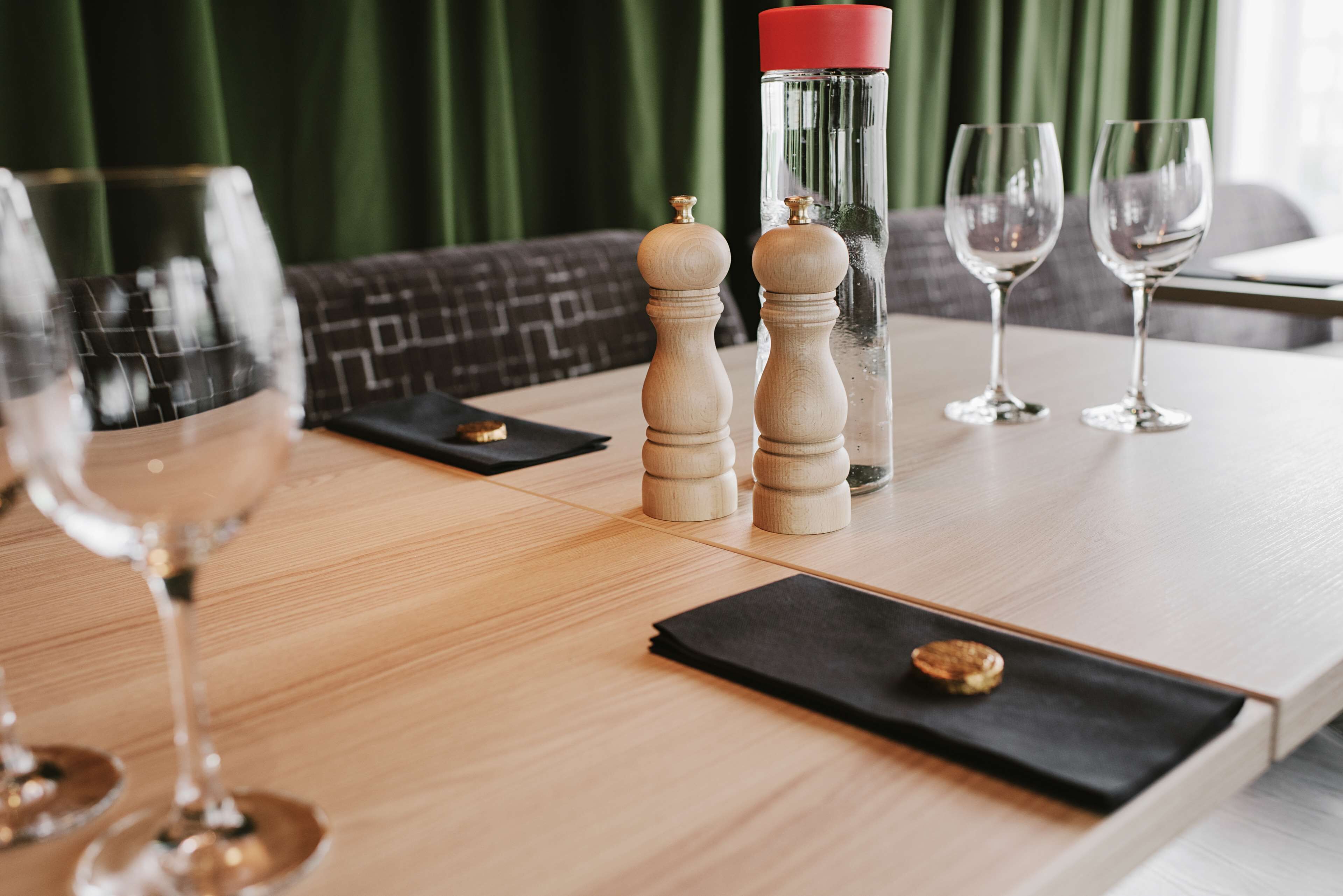 A wooden table with two salt and pepper shakers, a glass bottle, and three wine glasses.