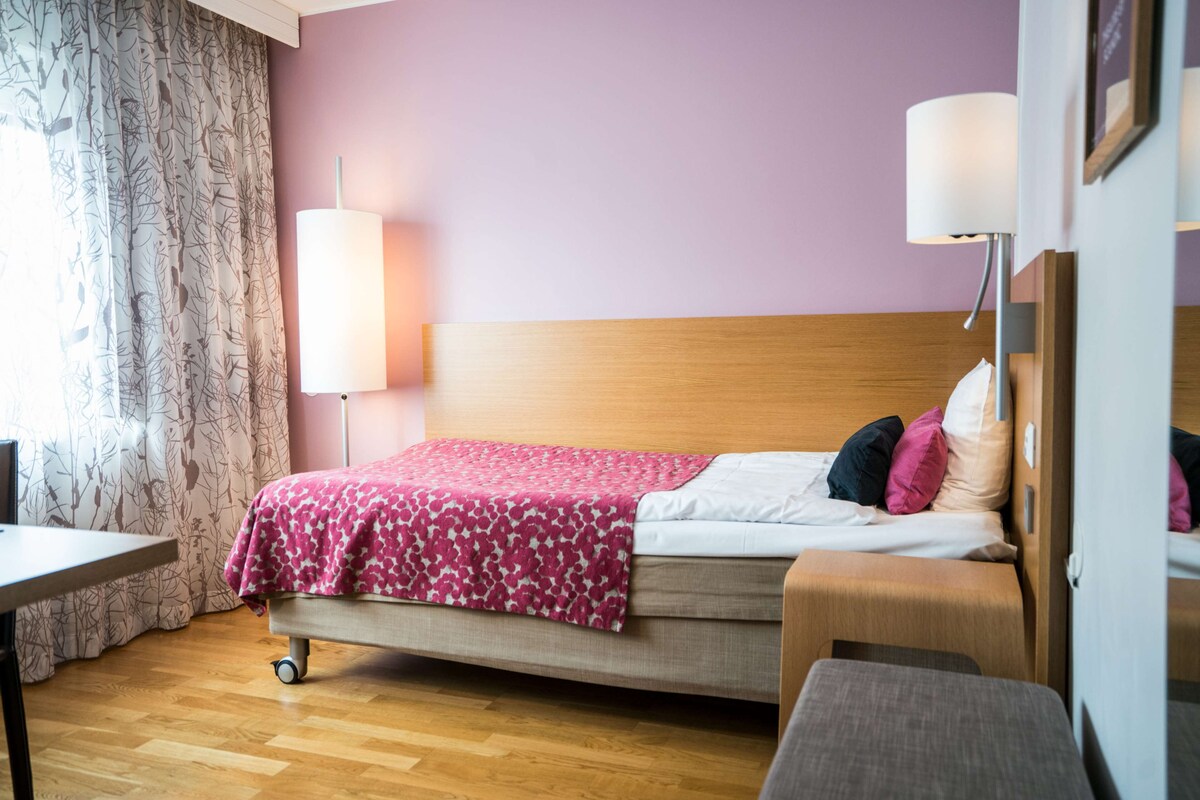 Una cama individual con cabecera, una mesita de noche, una lámpara y una silla en una habitación con suelo de madera y pared morada.