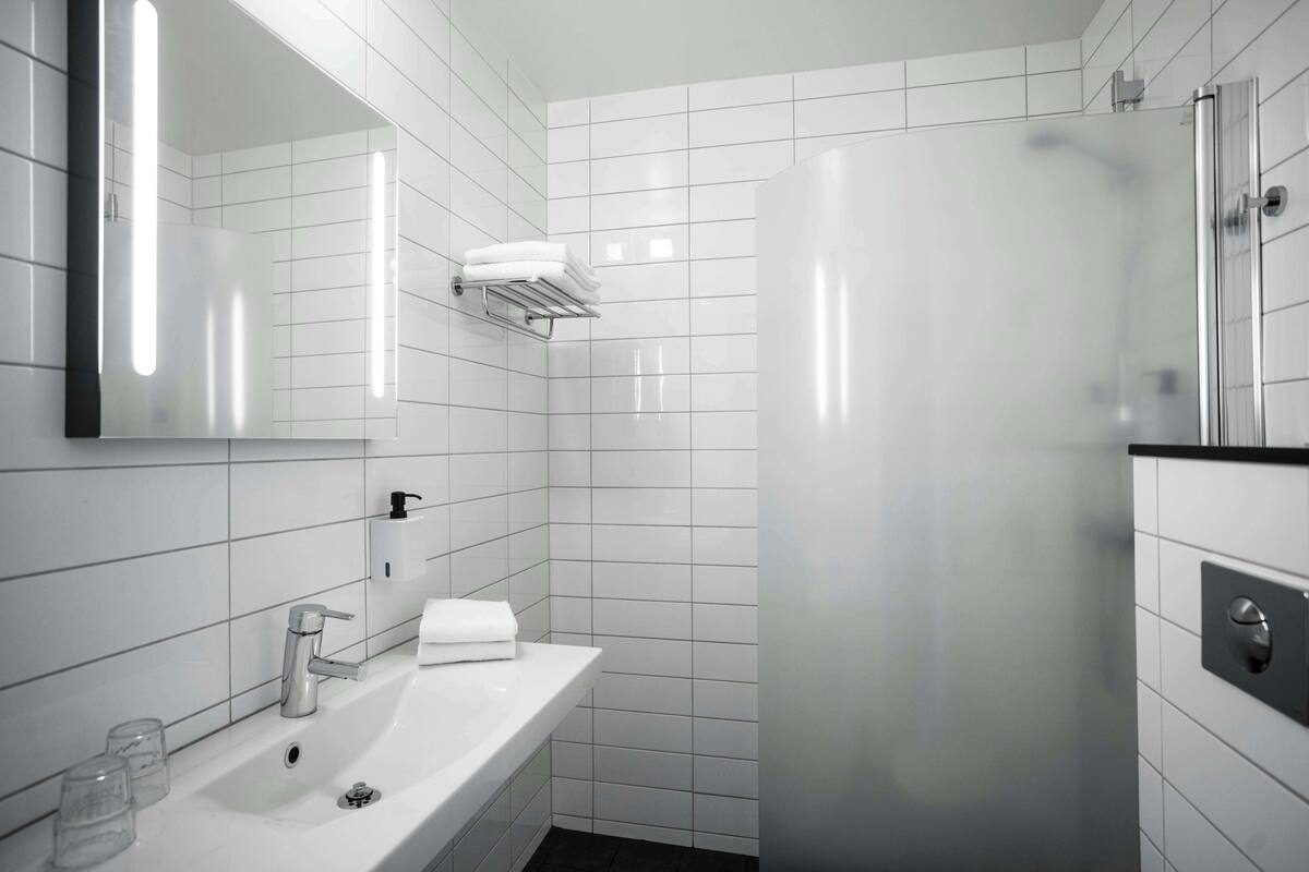 Un bagno moderno con un lavandino bianco, uno specchio, un appendi asciugamani e una cabina doccia in vetro.
