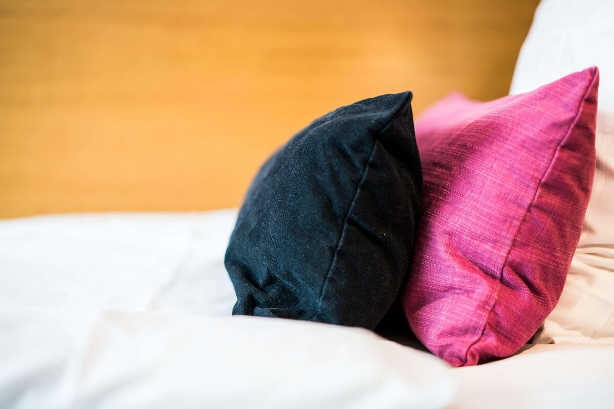 A bed with two pillows, one black and one pink, against a blurred background.