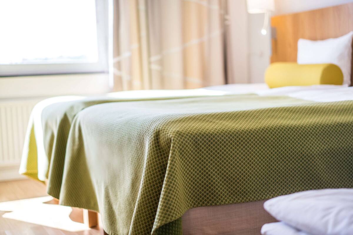 Camera d'albergo con due letti, una finestra con tende e una testiera in legno.