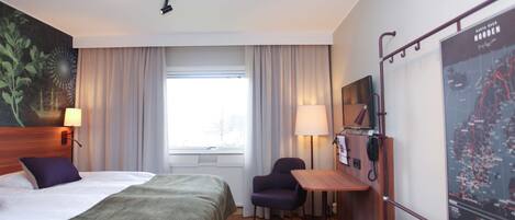 A hotel room with a bed, a desk, a chair, a map on the wall, and a window with curtains.