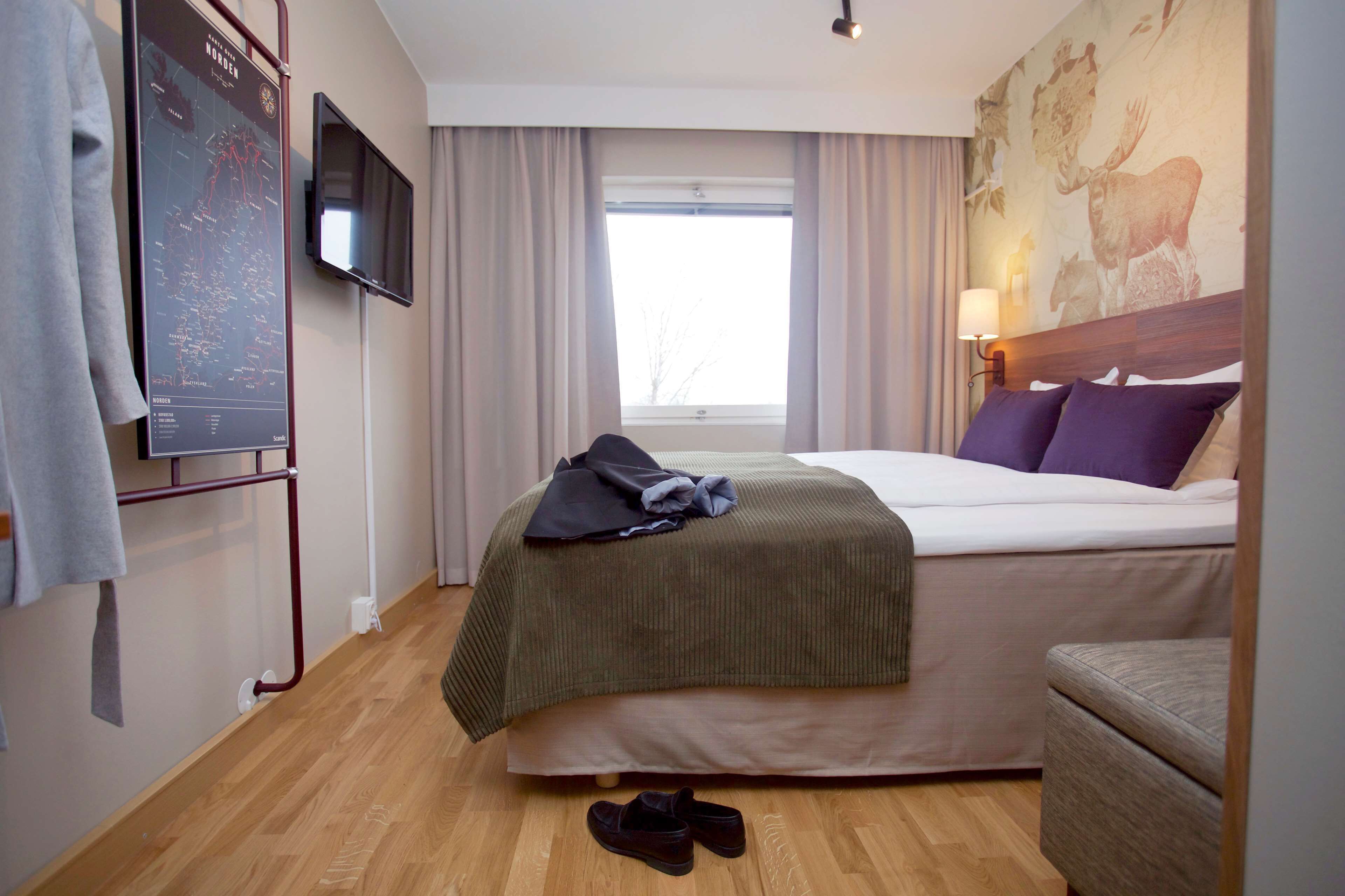 A hotel room with a bed, a TV mounted on the wall, a window with curtains, and a map on the wall.