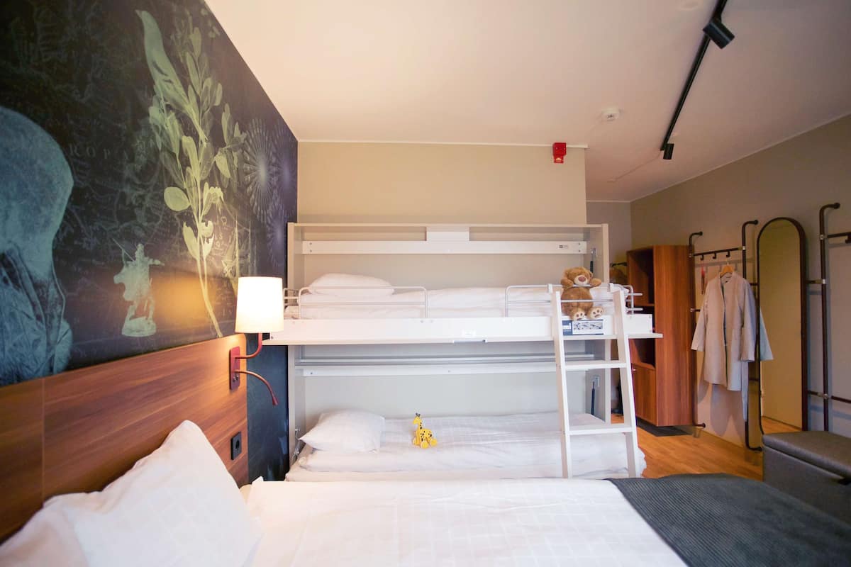 A bunk bed room with a wooden headboard, a wall-mounted lamp, and a shelf with a teddy bear.