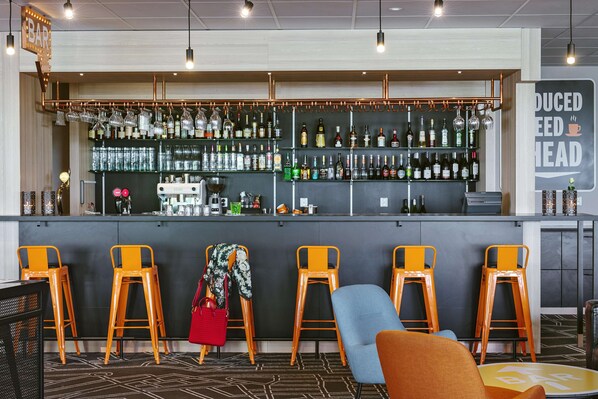 A bar area with multiple stools, a counter with various bottles, and a sign indicating a reduced head fee. - Scandic Klarälven (Karlstad)