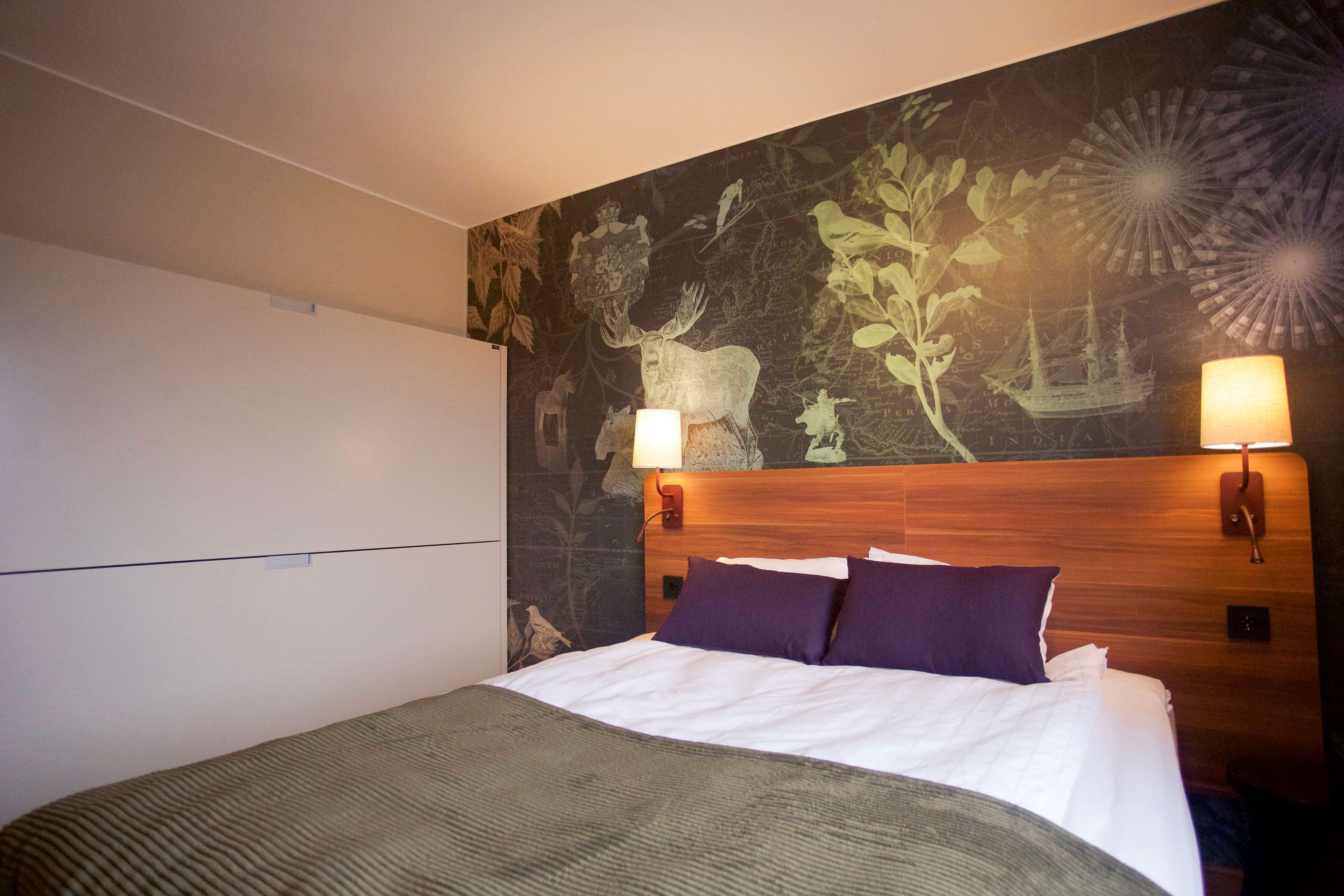 Una habitación de hotel con una cama, un cabecero con decoración de pared y dos lámparas fijadas a la pared.