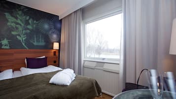 Una habitación de hotel con una cama, un ventanal grande, una lámpara de pared y un cuadro.