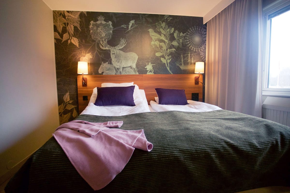 A hotel room with a large bed, two bedside lamps, and a mural on the wall.