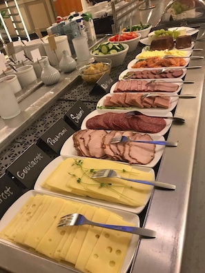 A buffet with various food items including sliced meats, cheese, and vegetables.