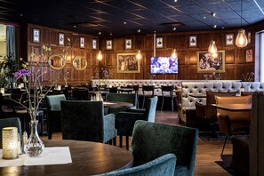 A restaurant with wooden panel walls, a large TV screen, and a variety of seating options including round tables and cushioned booths.