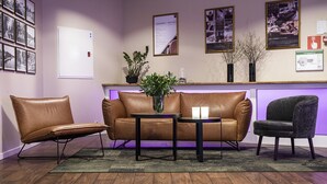 A reception area with a brown leather sofa, two armchairs, a small table with a vase, and a wooden floor. - First Hotel Royal (Saffle)