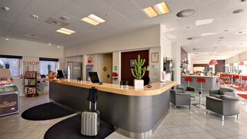 A modern hotel lobby with a reception desk, seating area, and a shop.