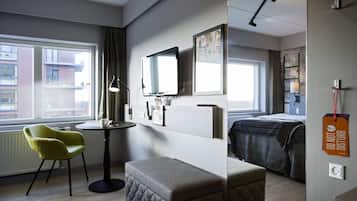 A hotel room with a bed, a small table with a chair, a TV, and a window with curtains.