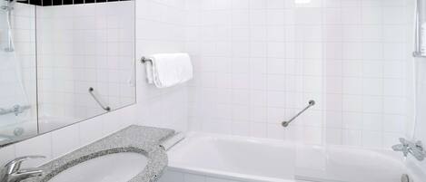 A modern bathroom with a granite countertop sink, a white bathtub, and a shower area.
