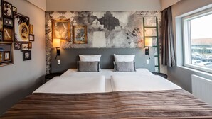 A hotel room with a large bed, two bedside tables, a wall-mounted lamp, and a view of parked cars through the window. - Scandic Olympic (Esbjerg)