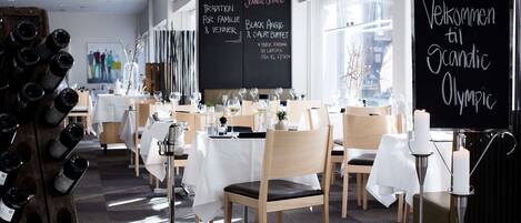 A restaurant with white tablecloths, wooden chairs, and a chalkboard menu.