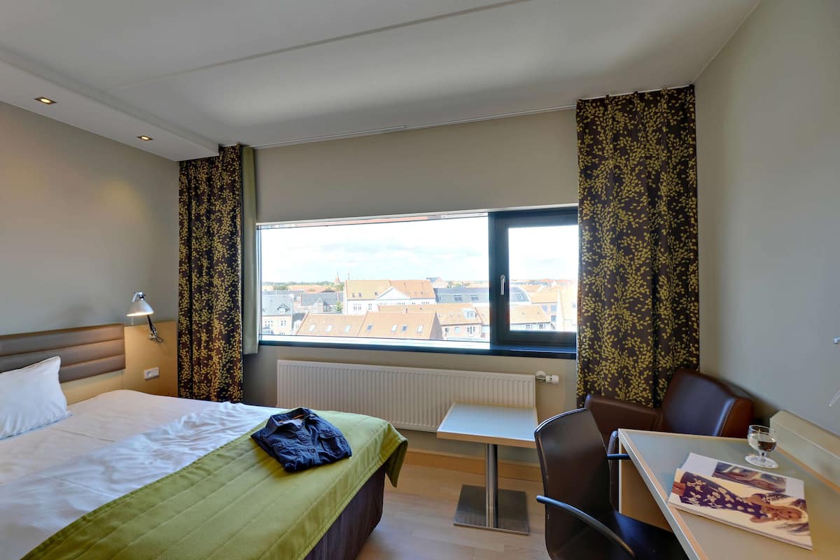 A hotel room with a bed, a desk, a chair, and a window with a city view.