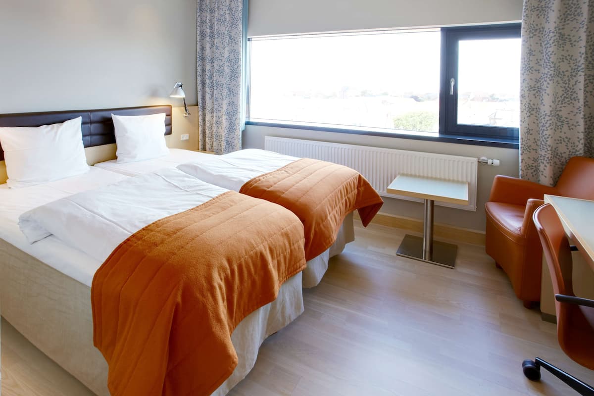 A hotel room with a large bed, a small table, and a chair.