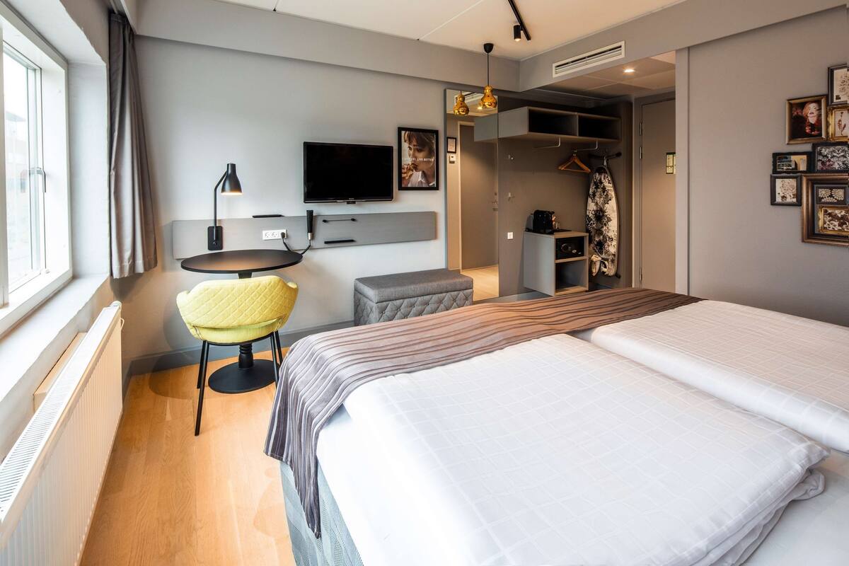 A modern hotel room with a bed, a desk, a chair, a TV, and a wardrobe.