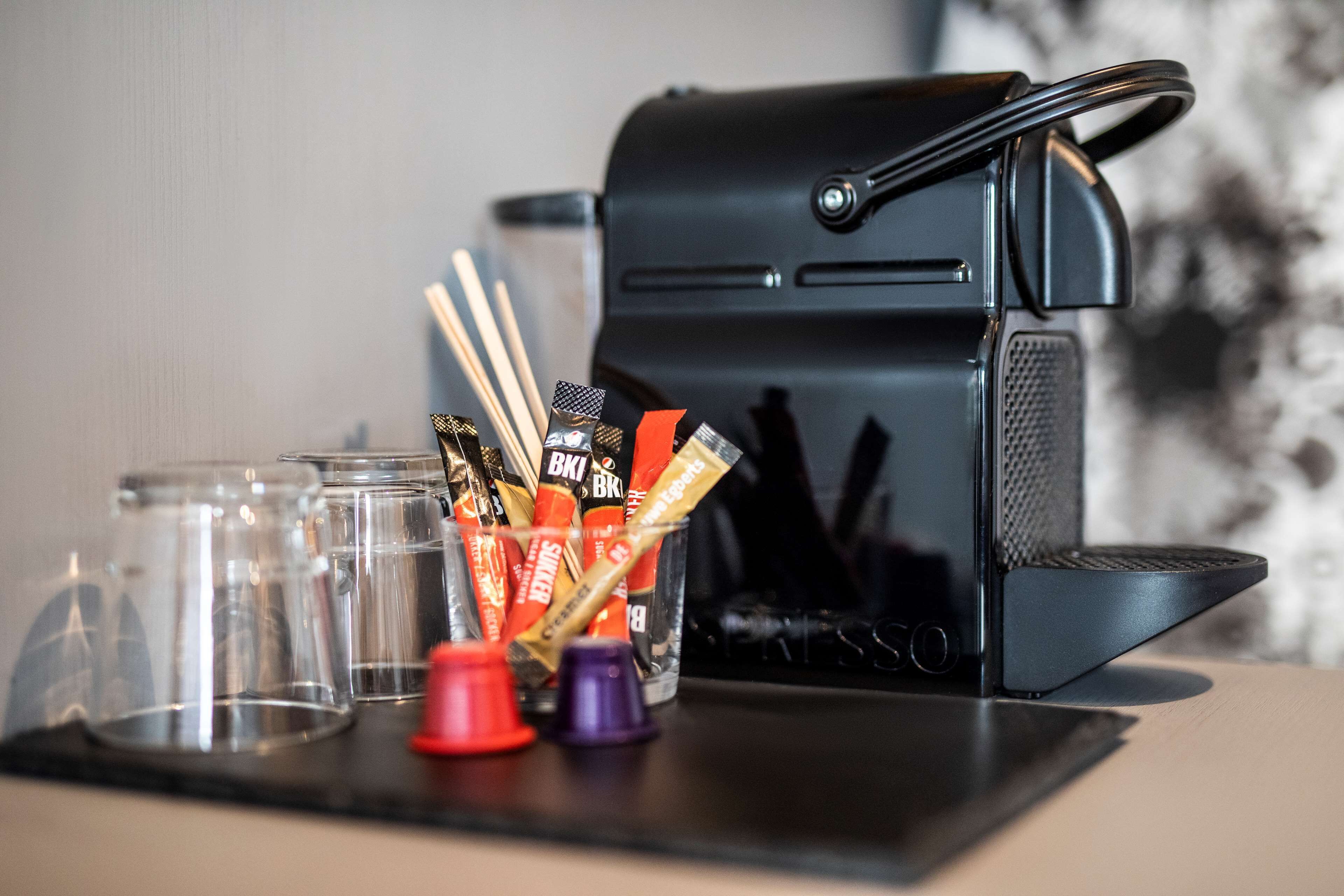 A coffee machine, a glass container with snacks, and a few glasses on a table.