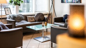 A modern living room with a glass coffee table, leather sofas, a potted plant, and a framed certificate on the windowsill. - Scandic Olympic (Esbjerg)