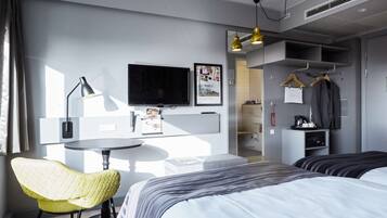 Una habitación de hotel moderna con cama, escritorio, silla, televisor y armario.