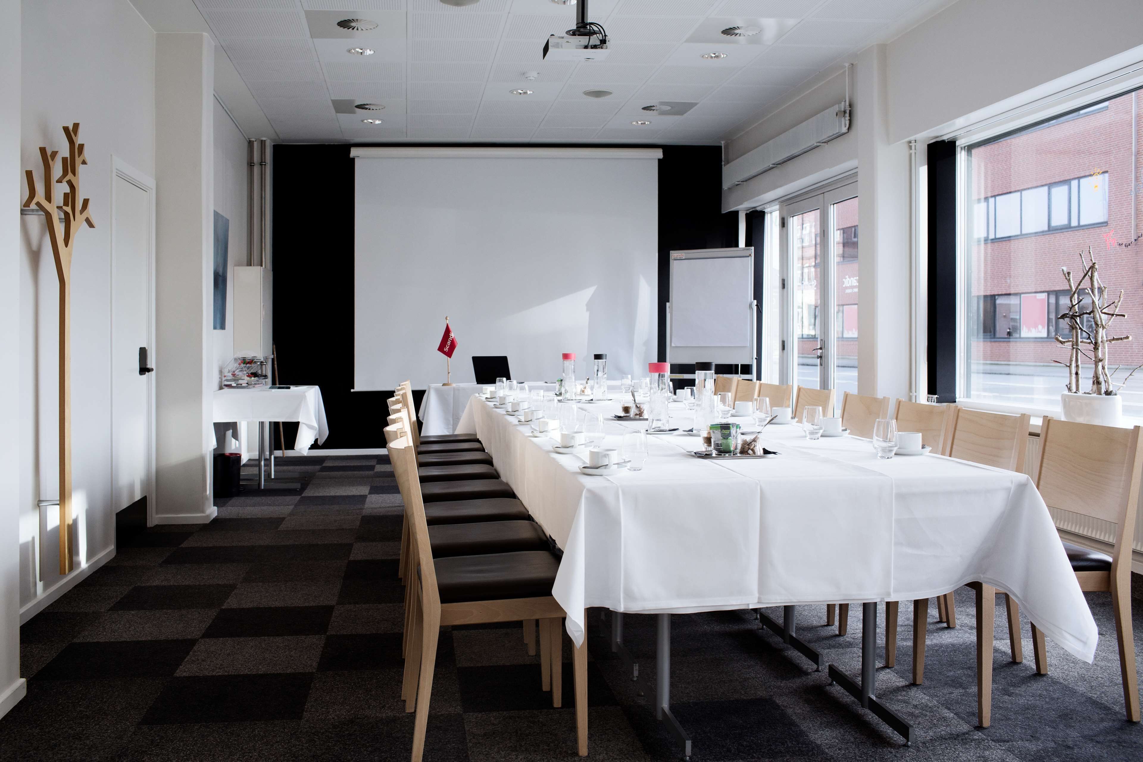 A conference room with a long table set for a meeting, equipped with chairs, a projector screen, and a whiteboard.