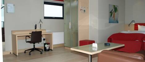 A modern hotel room with a wooden desk, a red sofa, a glass table, and a red chair.