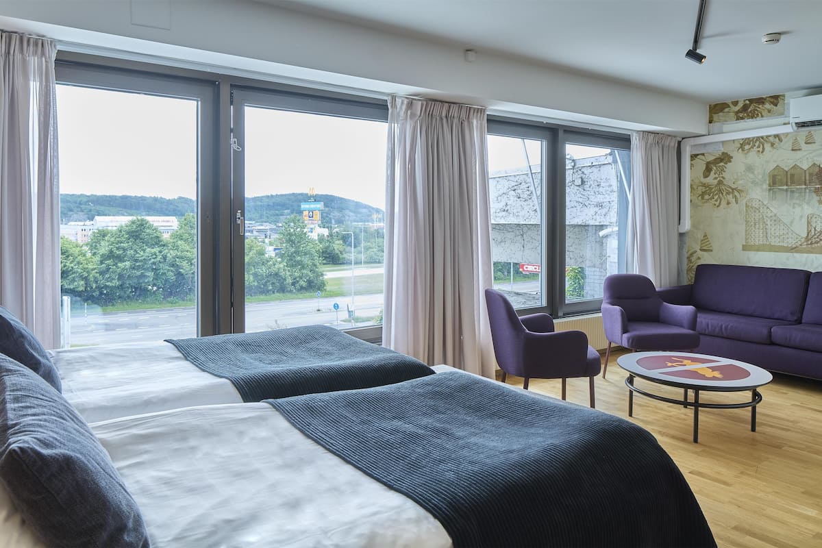 Ett hotellrum med en stor säng, två stolar, ett litet bord och utsikt över omgivningarna.