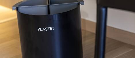 Une poubelle noire en plastique, sur laquelle est inscrit le mot « PLASTIQUE », est posée sur un plancher en bois.