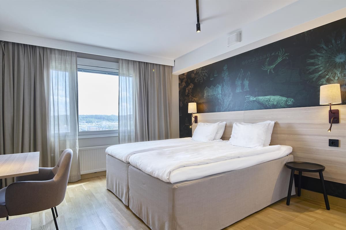 Ett hotellrum med en säng, ett skrivbord, en stol, en tv och ett fönster med gardiner.