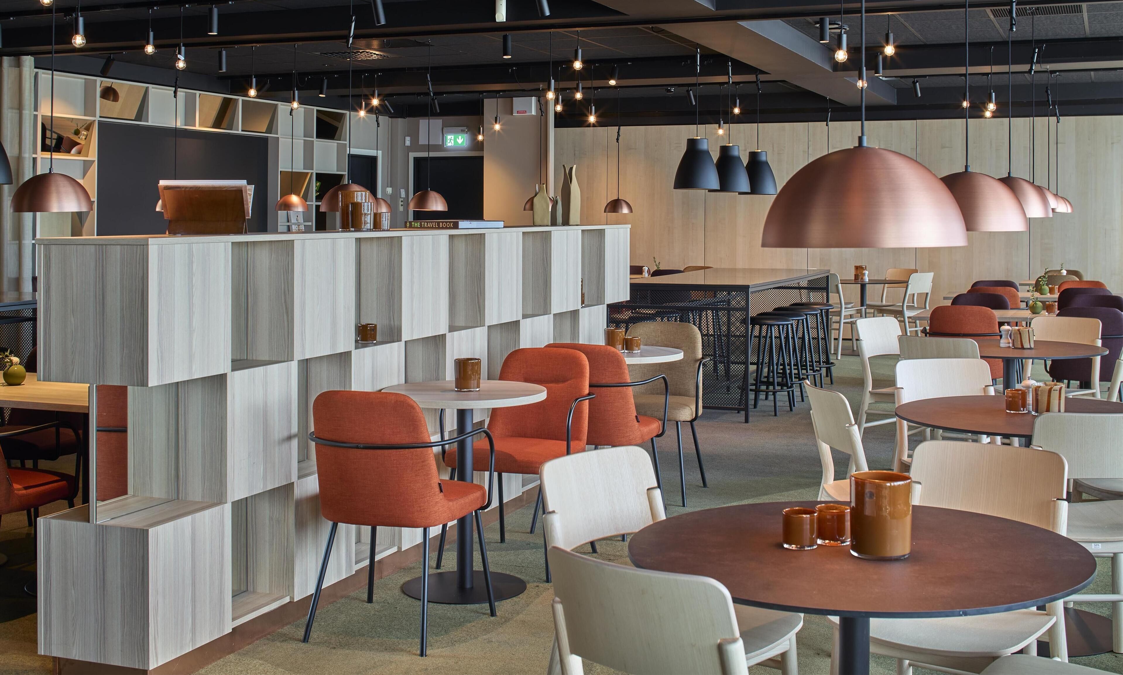 A modern restaurant interior with high ceilings, pendant lighting, and a mix of round and square tables.