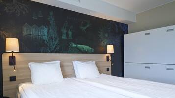 A hotel room with a bed, two wall-mounted lamps, a large tapestry, and a minibar.