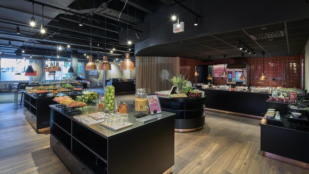 A modern hotel lobby with a buffet area, wooden flooring, and pendant lighting. - Scandic Backadal (Hisings Backa)