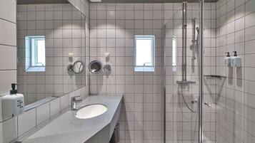 Un baño moderno con un lavamanos grande, un espejo, un secamanos y una zona de ducha con mampara de vidrio.