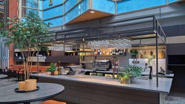 Un área de bar moderna con mostrador, taburetes y una zona de estar con mesas y sillas.