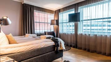 A modern hotel room with a large bed, a flat-screen TV, and a view of the city through large windows.