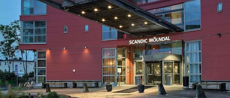 A modern building with a red facade, large glass windows, and a covered entrance.