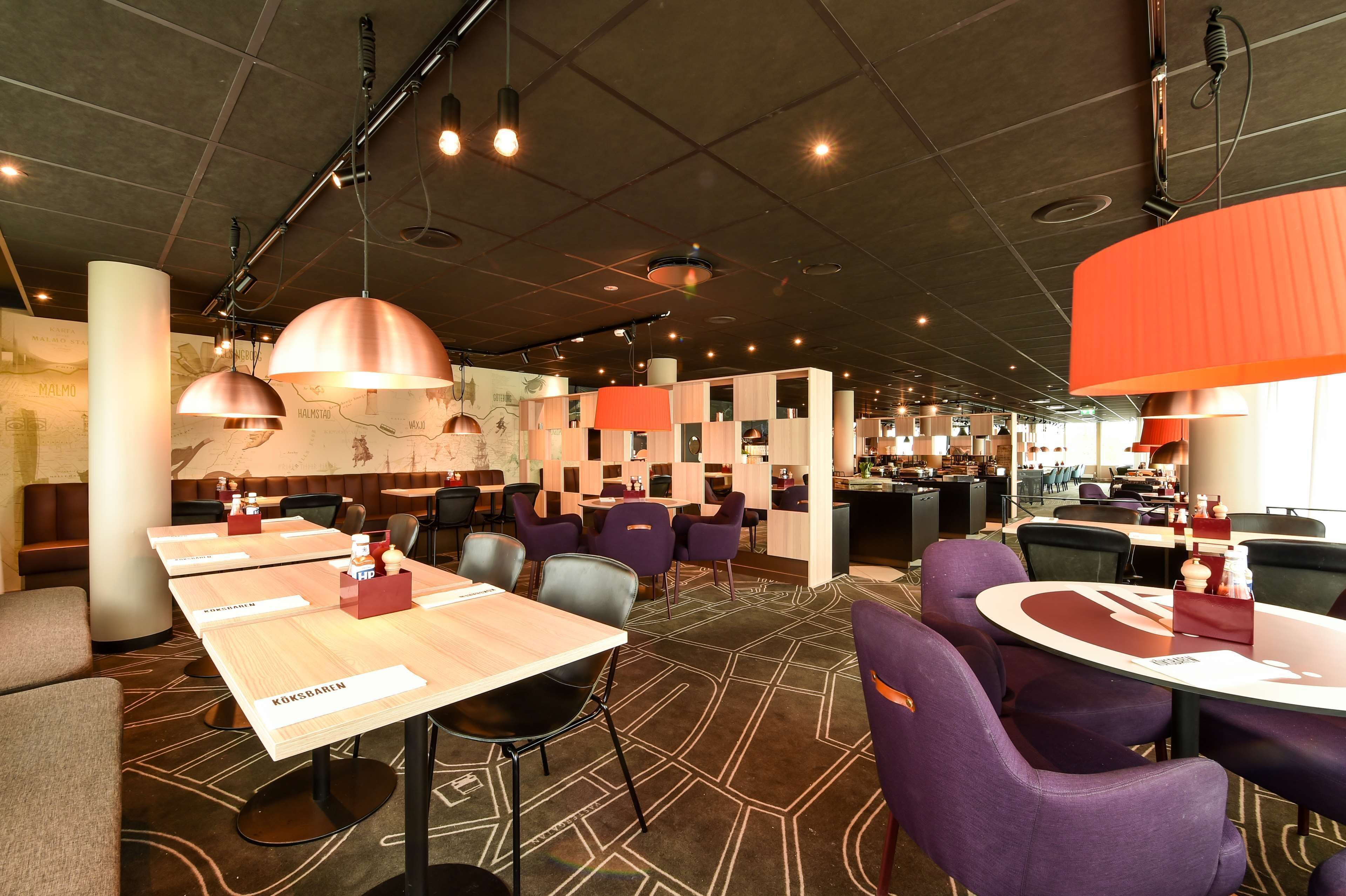 En modern restaurang med flera olika sittområden, inklusive avskilda bås och runda bord, samt en bardisk i bakgrunden.