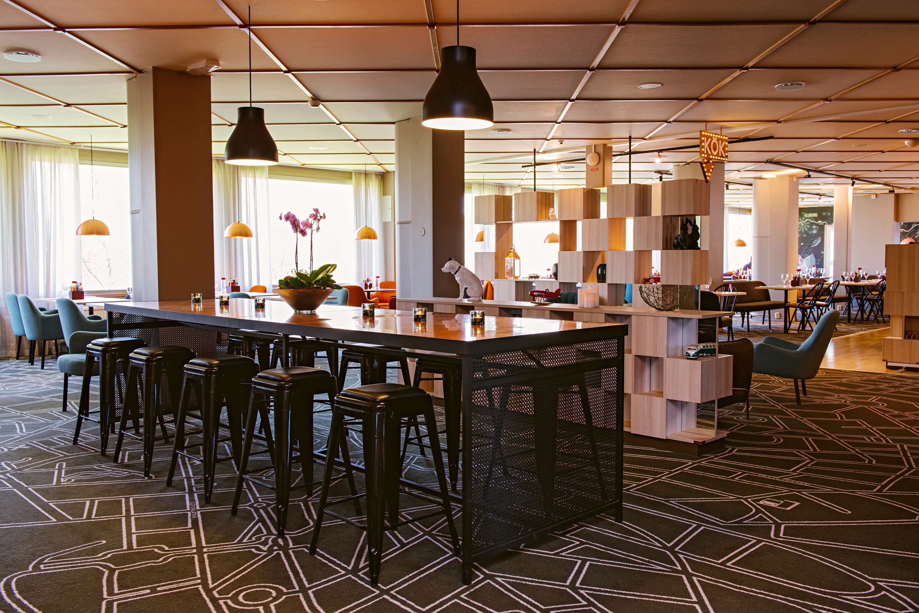 A modern bar area with a central island, multiple bar stools, pendant lighting, and a patterned carpet.